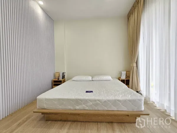 Townhouse for sale in Lat Phrao, Bangkok - Minimal master bedroom with platform bed and full-height curtains.