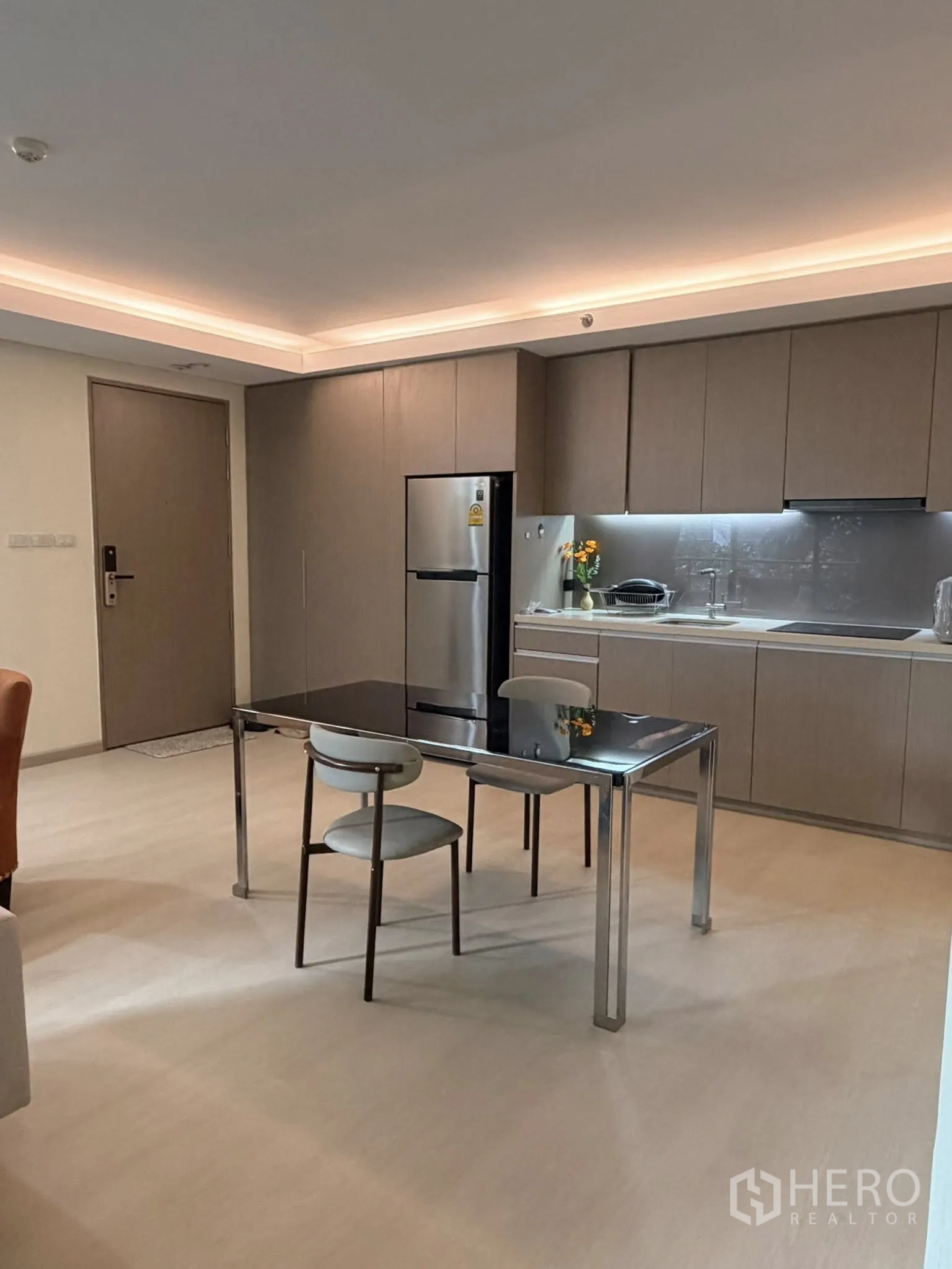 Condominium for rent in Watthana, Bangkok - Open-plan kitchen with full-height cabinets, fridge, and a dining table for two.