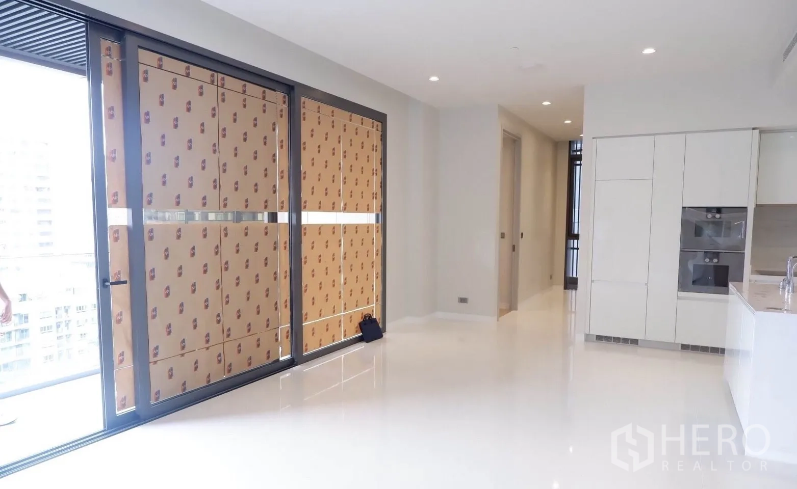 Condominium for sale in Watthana, Bangkok - Open-plan living and white kitchen with built-in ovens and sliding doors to the balcony.
