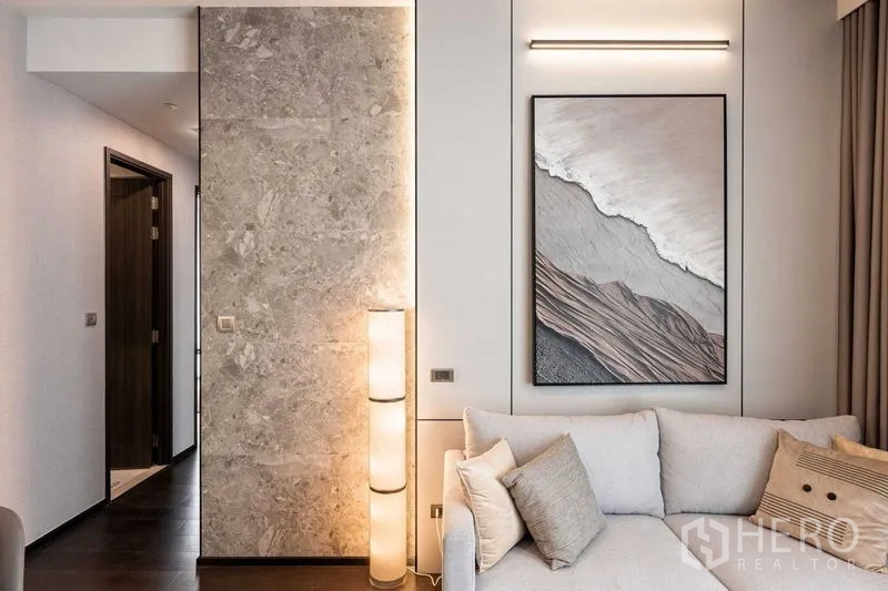Condominium for rent in Watthana, Bangkok - Cozy sofa corner with textured stone feature wall, floor lamp and framed artwork.