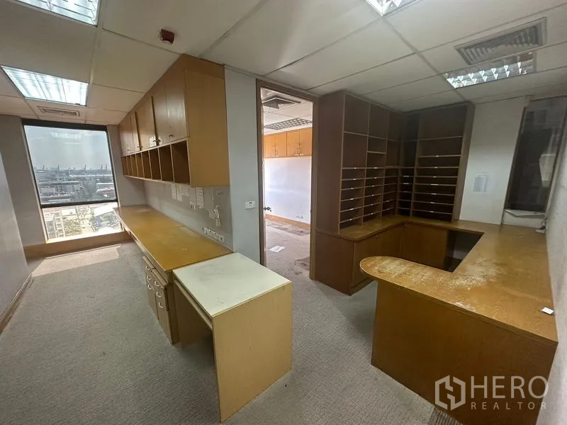 Office Space for rent in Khlong Toei, Bangkok - Private office with built‑in wooden cabinets, an L‑shaped workstation, and a window overlooking the skyline.