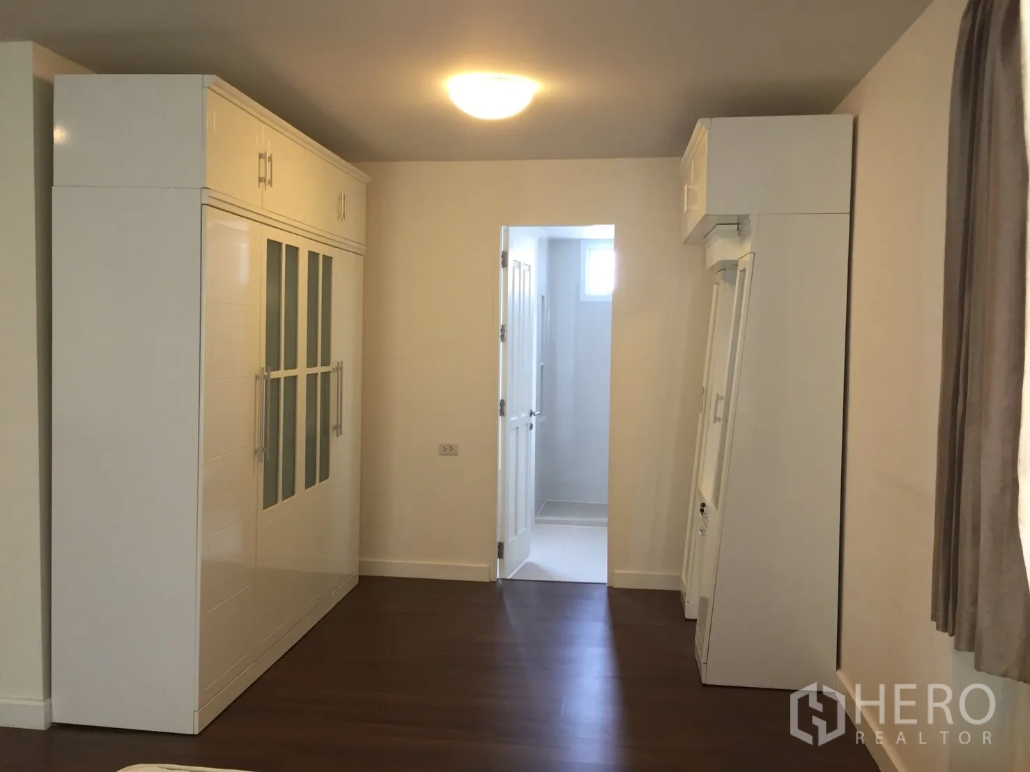 Townhouse for rent in Watthana, Bangkok - Bedroom corridor with built-in white wardrobes, wood flooring, and door to an en-suite bathroom.