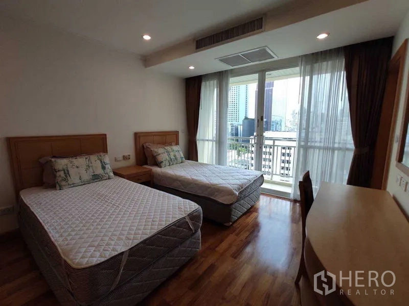 Condominium for rent in Khlong Toei, Bangkok - Bright bedroom with two single beds, wood floors and a balcony with city views through floor‑to‑ceiling windows.