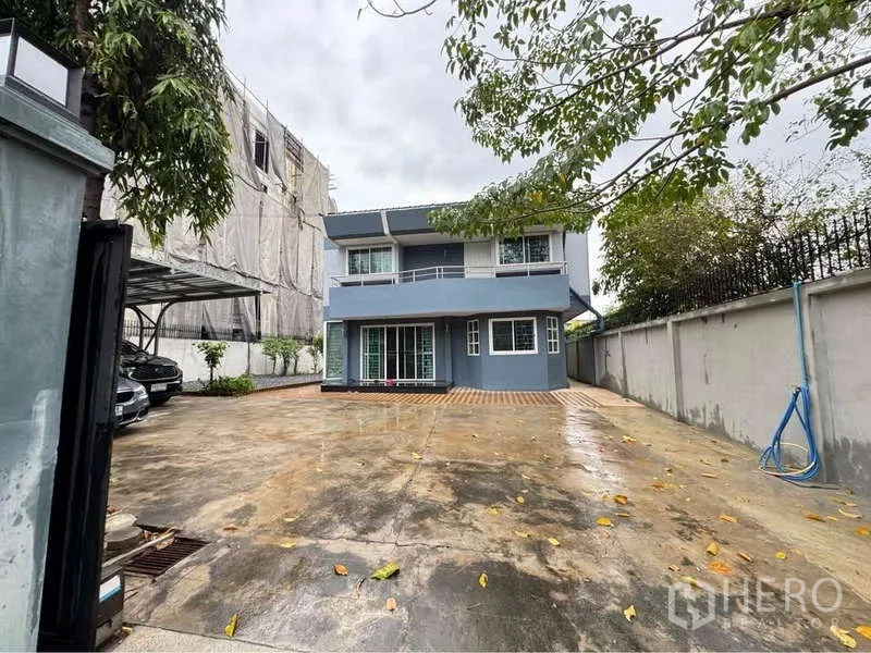 独立式住宅 出租在Suan Luang, Bangkok - 两层独栋别墅，前院宽阔混凝土车道，侧边有车棚与大门。