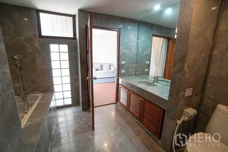Apartment for rent in Watthana, Bangkok - Marble-tiled bathroom featuring a bathtub, long vanity and large mirror.