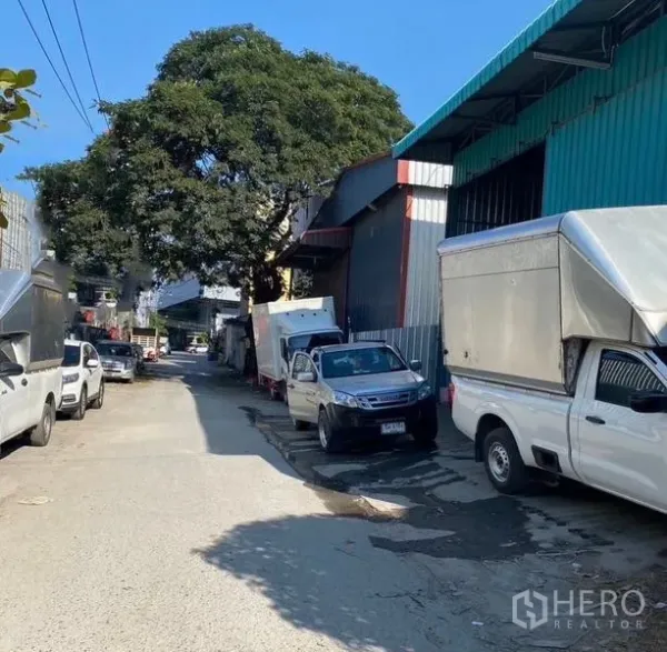 Warehouse for rent in Bang Kapi, Bangkok - Street view of a teal metal-clad warehouse in Bang Kapi with pickup trucks parked along the loading-friendly lane.