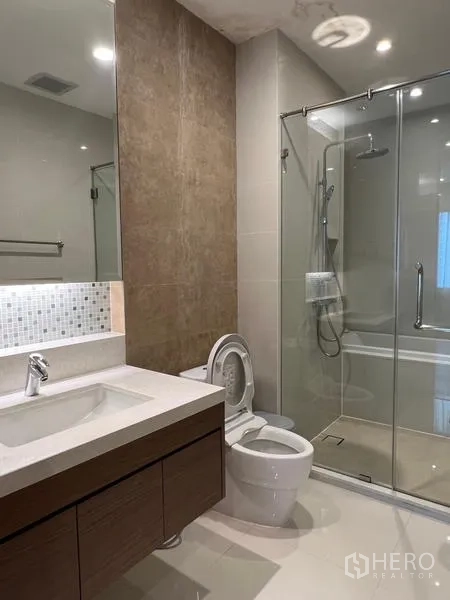 Condominium for rent in Khlong Toei, Bangkok - Modern bathroom with vanity, toilet and glass shower enclosure beside the bathtub.