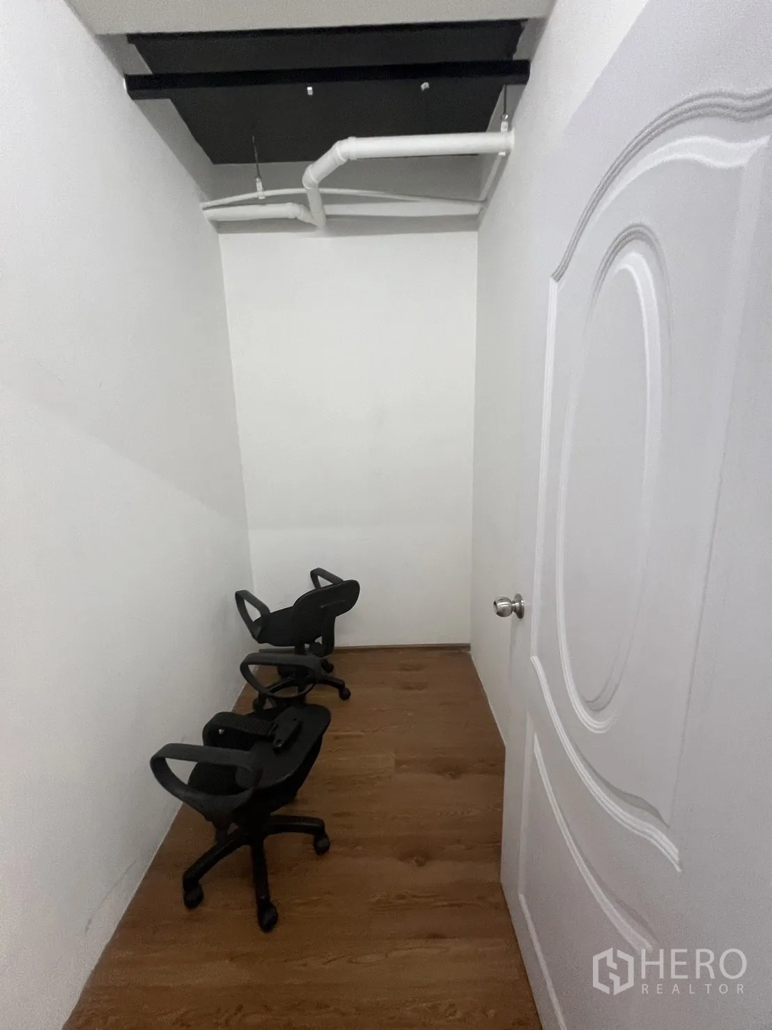 Office Space for rent in Khlong Toei, Bangkok - Narrow storage or server room with white walls, overhead pipes and a few office chairs.