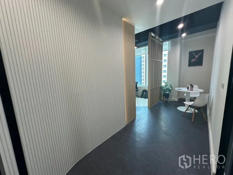 Office Space for rent - Curved hallway leading to lounge corner with round table, chairs and city windows.