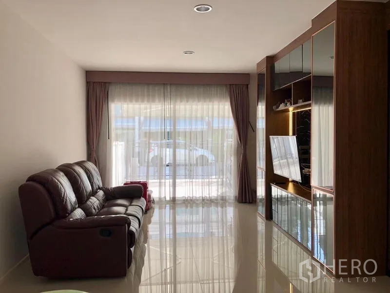 Townhouse for rent in Suan Luang, Bangkok - Bright living area with dark leather sofa, glossy tile floors and full-height curtains.