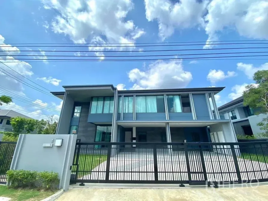 Detached House for sale in Bang Kapi, Bangkok - Front gate view of a two-storey detached house with a wide driveway and landscaped edges.