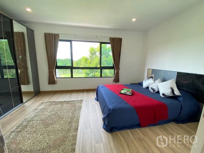 Townhouse for rent in Bang Kapi, Bangkok - Spacious master bedroom with wood flooring and a wide green view through a large window.