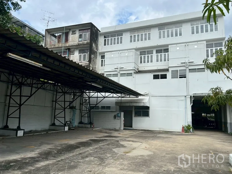 Shophouse for rent in Phra Khanong, Bangkok - Back elevation of the building overlooking a wide parking area and canopy.