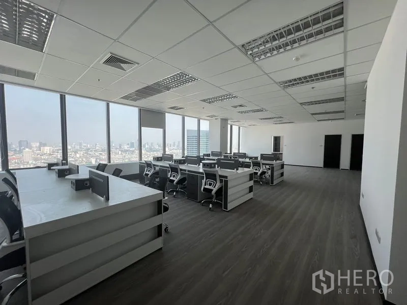 Office Space for rent in Huai Khwang, Bangkok - Open-plan workspace with bench desks and rolling chairs facing large windows and city views.