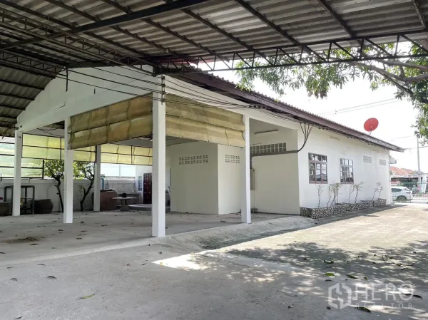 工厂 出租或出售在Pathum Thani - 带雨棚的装卸区，连接单层办公室与条纹遮阳篷。