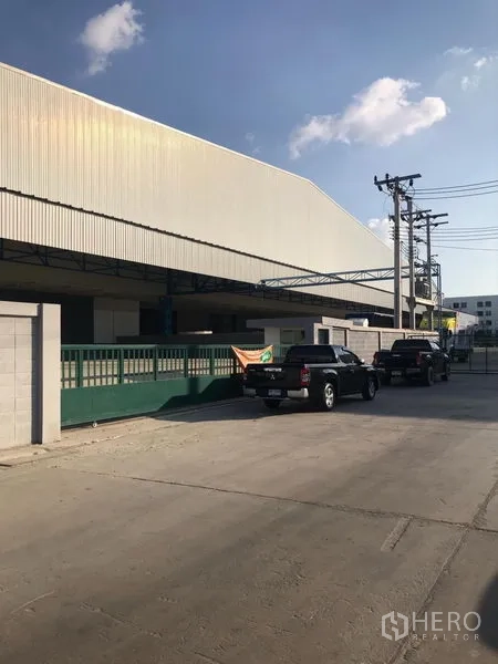 货栈 出租在Samut Prakan - 仓库外观街景，金属板立面、绿色大门与带雨棚的装卸区，位于邦梭通。