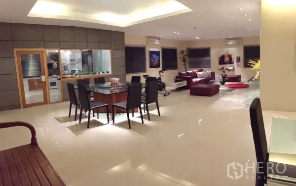 Condominium for rent in Bang Rak, Bangkok - Open-plan living and dining area with glossy floors, glass-walled kitchen, and a red leather sofa.