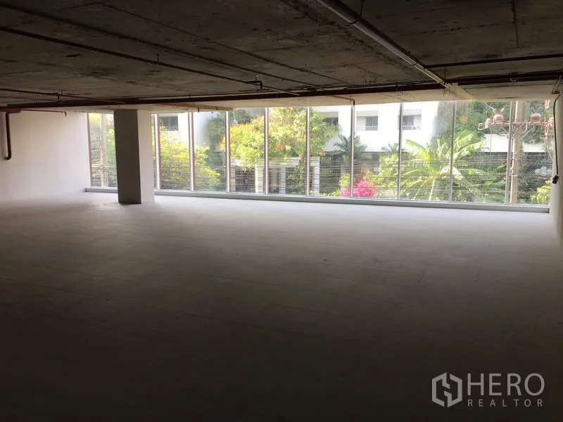 Retail Space for rent in Khlong Toei, Bangkok - Wide retail space facing a long glass facade with garden views, structural column, and smooth tiled flooring.