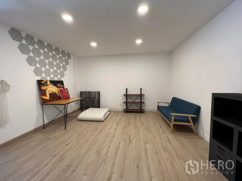 Townhouse for rent in Ratchathewi, Bangkok - Flexible studio room with wood-look floors, recessed lighting, sofa and shelving.