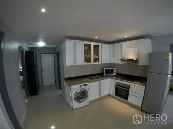 Condominium for rent in Watthana, Bangkok - Modern L-shaped kitchen with white cabinets, oven, cooktop, washing machine and fridge.