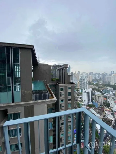 Condominium for rent or sale in Khlong Toei, Bangkok - Balcony with metal railing overlooking a neighboring condominium tower and Bangkok skyline on a cloudy day.