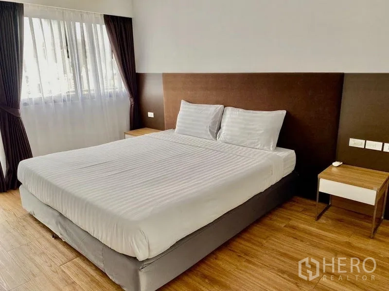 Condominium for rent in Khlong Toei, Bangkok - Guest bedroom with large bed, brown upholstered headboard and side tables.