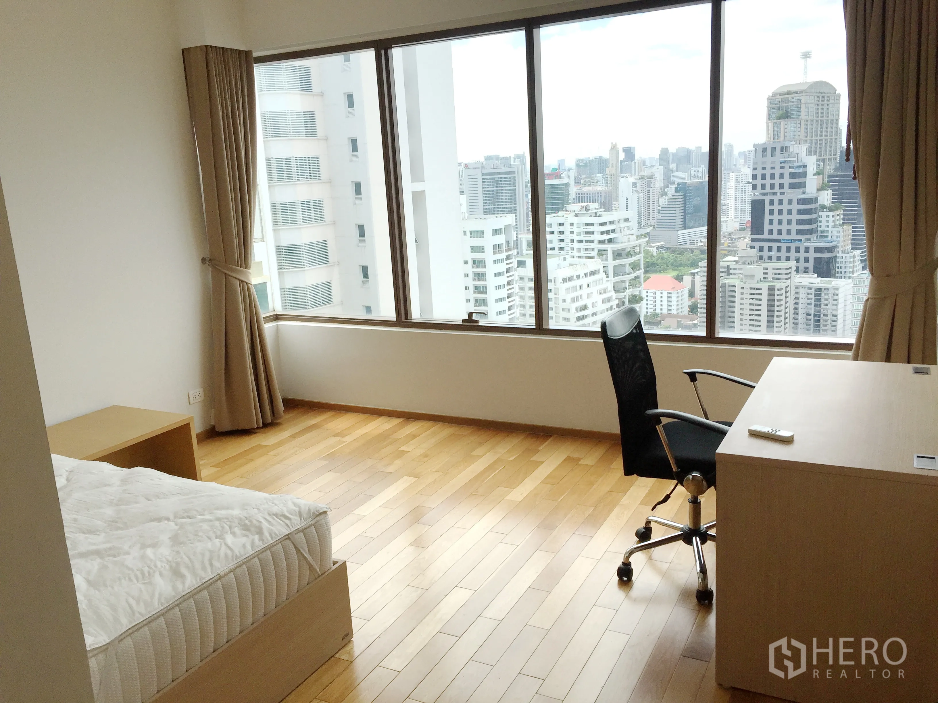 Condominium for rent in Khlong Toei, Bangkok - Bright bedroom with desk and panoramic city skyline views through wide windows and light wood floors.