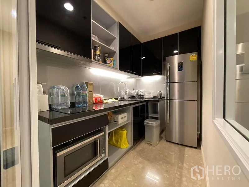 Condominium for sale in Khlong Toei, Bangkok - Galley kitchen with black cabinetry, under-cabinet lighting, stainless fridge and microwave.
