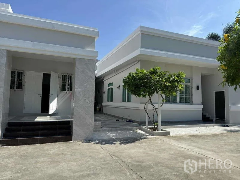 独立式住宅 出租在Samut Prakan - 现代单层住宅外观，铺装车道与小树。