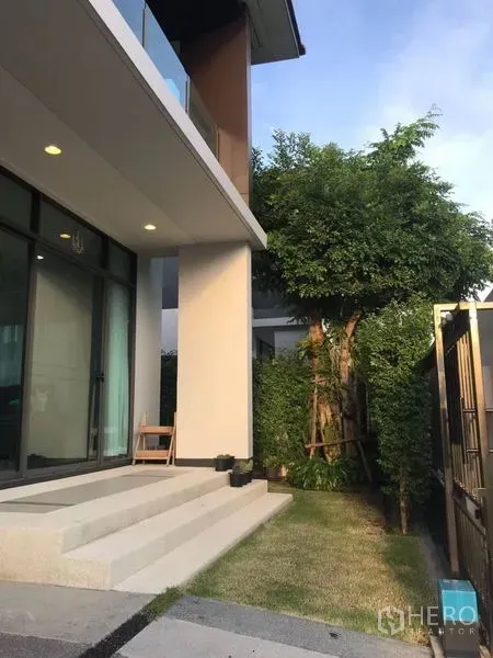 บ้าน ให้เช่าในBang Kapi, Bangkok - บันไดหน้าบ้านและสวนข้างบ้าน มีต้นไม้ใหญ่ ข้างประตูกระจกและหน้าต่างสูง