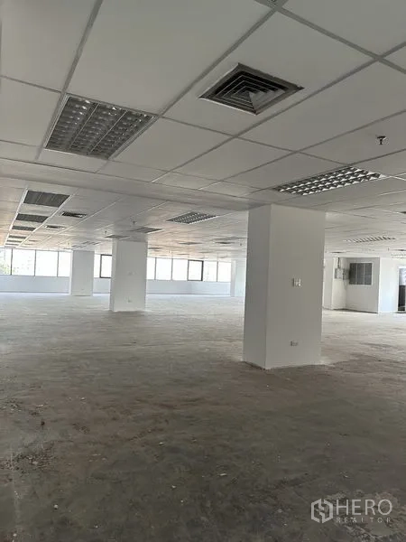 办公空间 出租在Pathum Wan, Bangkok - 空置办公室内景，网格吊顶、照明与通风口，结构柱清晰可见。