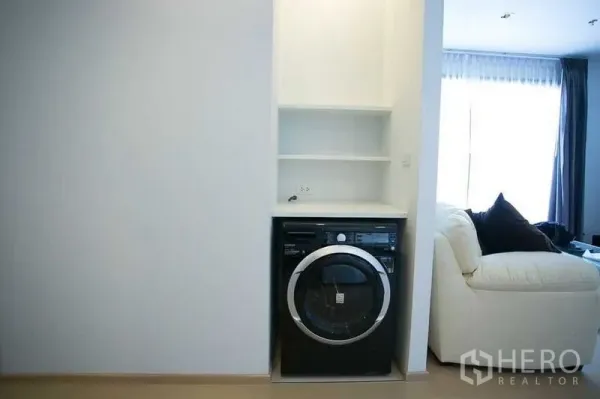 Condominium for rent in Watthana, Bangkok - Built-in laundry nook with front-load washer beside a bright living area in a Thonglor condo.