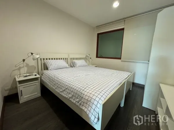 Condominium for rent in Pathum Wan, Bangkok - Cozy bedroom with white bed frame, grid-pattern bedding, and bedside lamps.