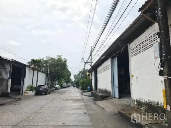 Warehouse for rent in Mueang Samut Prakan, Samut Prakan - Industrial lane lined with warehouses, overhead power lines and truck-friendly access in a quiet estate.