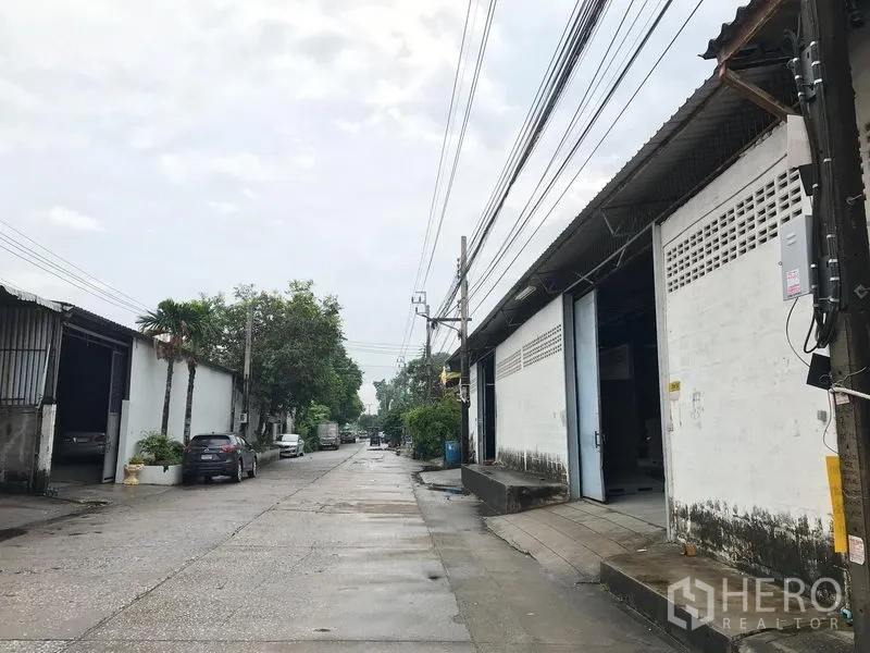 Warehouse for rent in Mueang Samut Prakan, Samut Prakan - Industrial lane lined with warehouses, overhead power lines and truck-friendly access in a quiet estate.