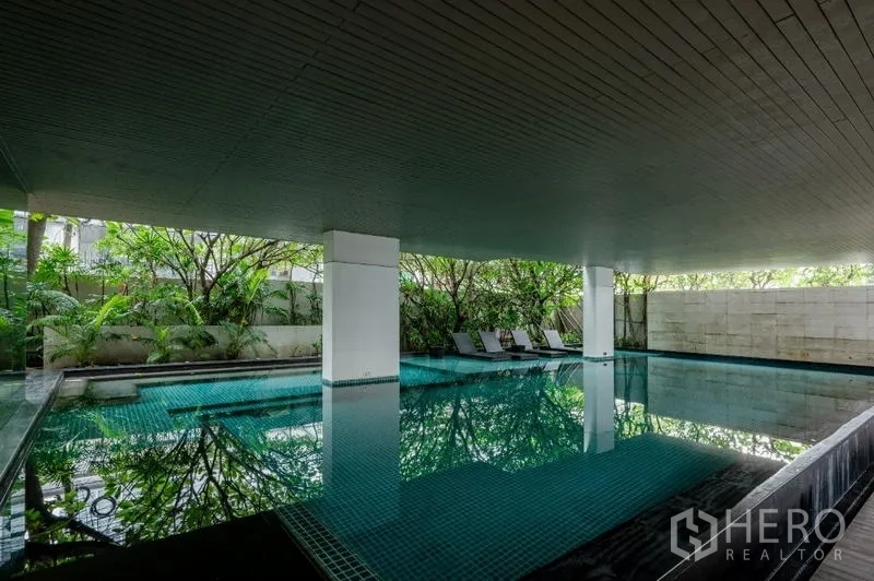 Condominium for sale - Covered swimming pool surrounded by lush greenery and sun loungers.