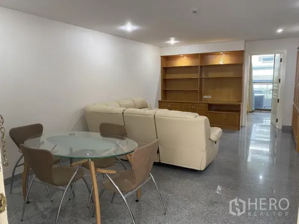 公寓 出租或出售在Watthana, Bangkok - 餐客一体空间，圆形玻璃餐桌与四把椅子，浅色沙发和内置电视柜，吊顶射灯。
