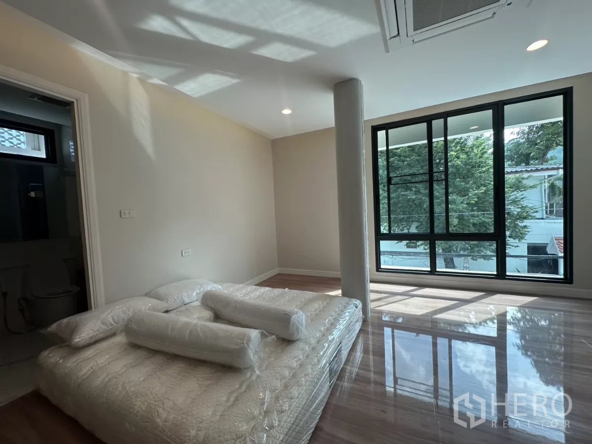 Townhouse for rent in Watthana, Bangkok - Corner bedroom with large windows, tree views, and a temporary mattress.
