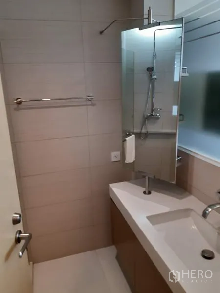 Condominium for rent in Khlong Toei, Bangkok - Contemporary bathroom with vanity, mirror, and glass shower enclosure.