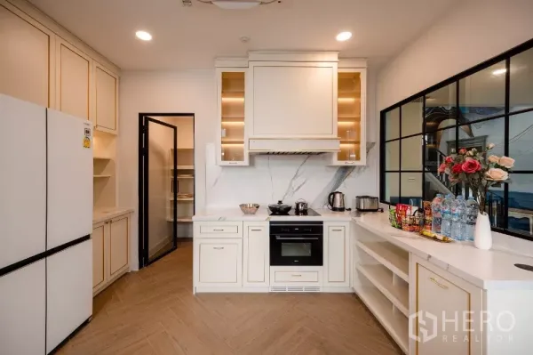 Detached House for rent or sale in Khlong Toei, Bangkok - Bright European-style kitchen with cream cabinetry, marble backsplash, oven and pantry door.