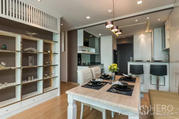 Condominium for rent in Watthana, Bangkok - Dining zone with pendant lights, white table, display shelves and an open kitchen with washer and breakfast bar.