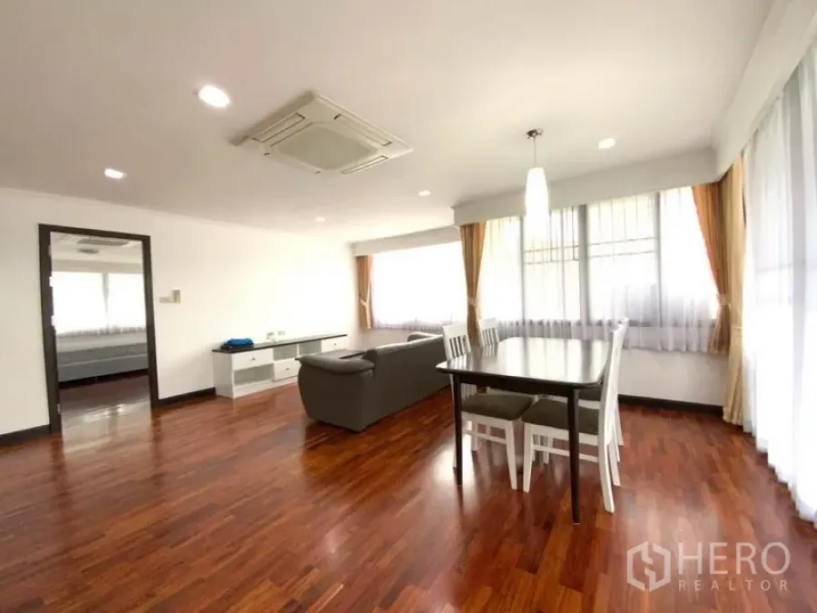 公寓 出租在Watthana, Bangkok - 采光充足的客餐一体空间，木地板，灰色沙发，白色餐桌，转角大窗与吊顶空调。