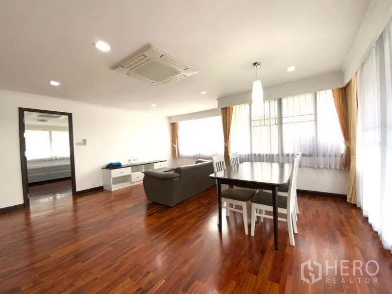 公寓 出租在Watthana, Bangkok - 采光充足的客餐一体空间，木地板，灰色沙发，白色餐桌，转角大窗与吊顶空调。