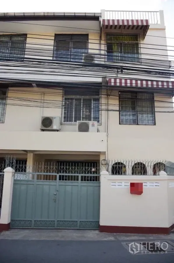 Townhouse for rent in Watthana, Bangkok - Three-storey townhouse facade with metal gate, striped awnings and exterior AC units.
