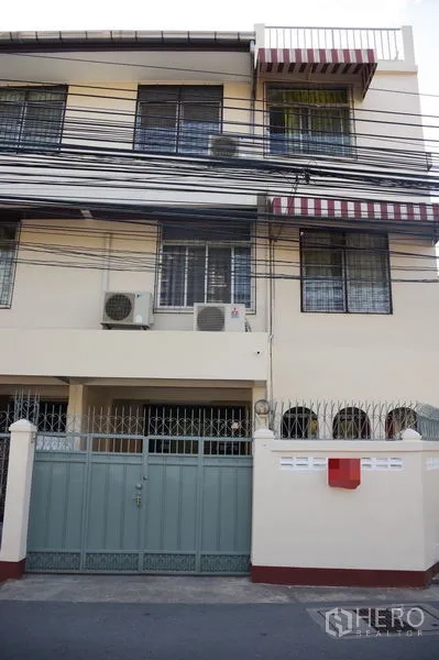 Townhouse for rent in Watthana, Bangkok - Three-storey townhouse facade with metal gate, striped awnings and exterior AC units.