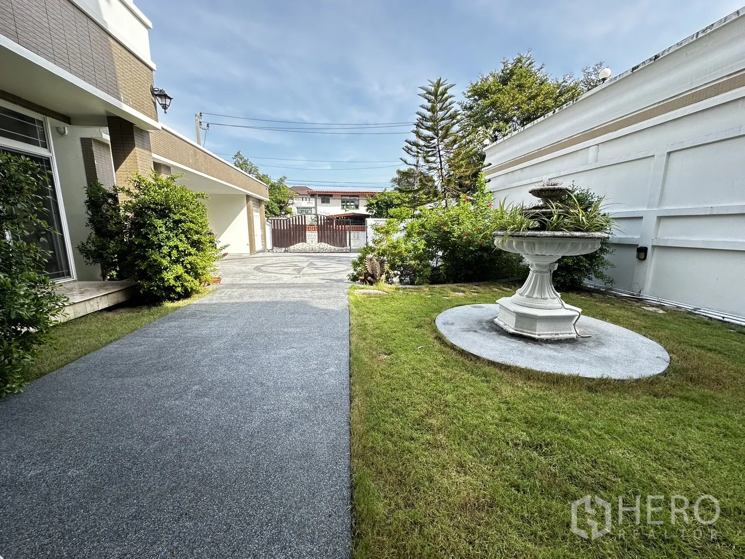 Detached House for rent in Chatuchak, Bangkok - Side garden with white fountain, lawn and pathway leading to the gated driveway.