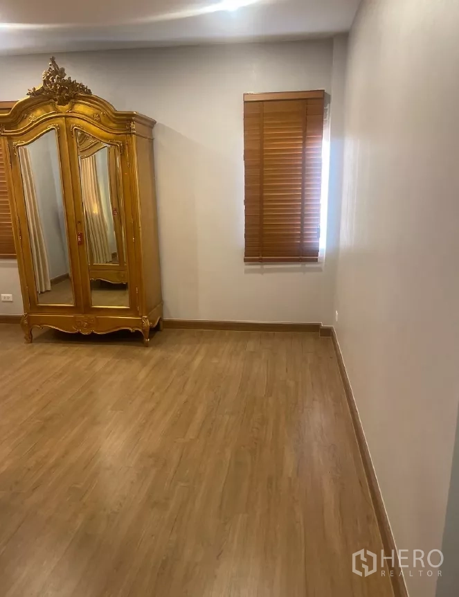 Detached House for rent or sale in Saphan Sung, Bangkok - Spacious bedroom with wood floors and a classic armoire.