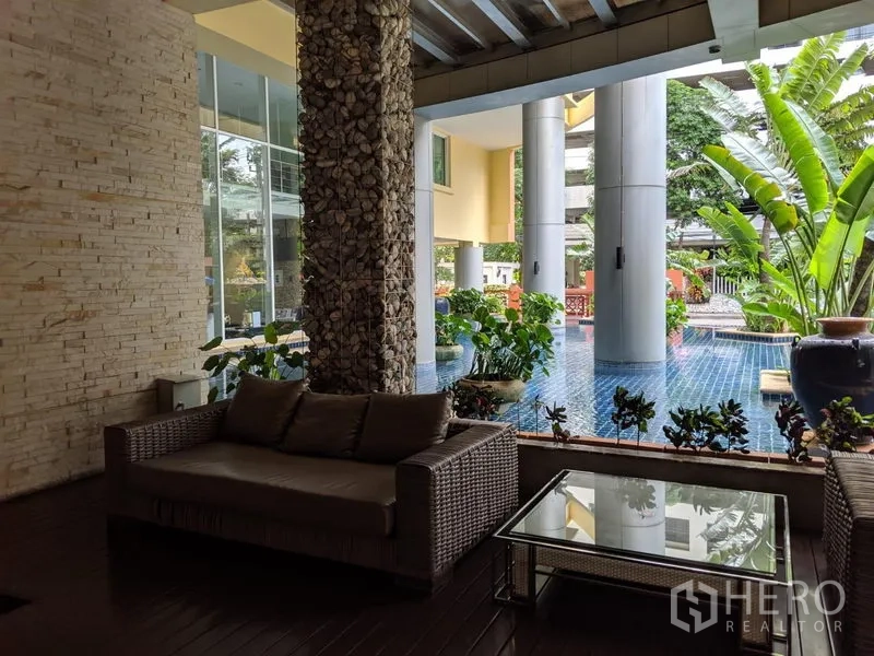 公寓 出租在Watthana, Bangkok - 半露天休闲区，藤编沙发、玻璃茶几与热带绿植临水而设。
