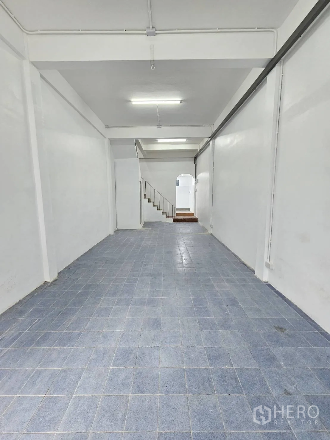 Home Office for rent in Khlong Toei, Bangkok - Long open-plan ground floor with white walls, blue floor tiles and ceiling lights.