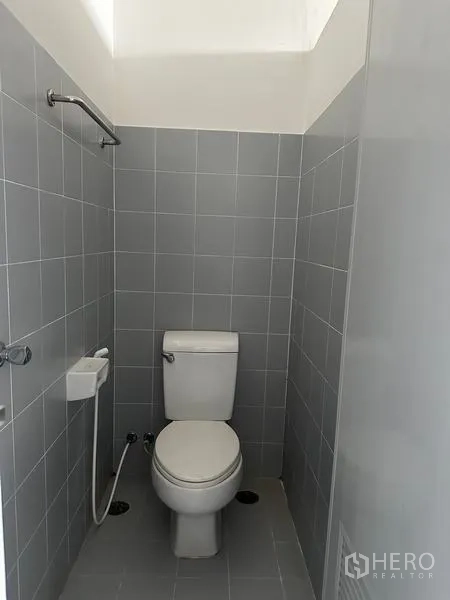 Factory for rent in Pathum Thani - Private toilet cubicle with bidet spray and grey wall tiles.
